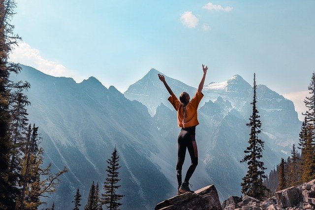woman with arms raised successfully hiked to top of trail 