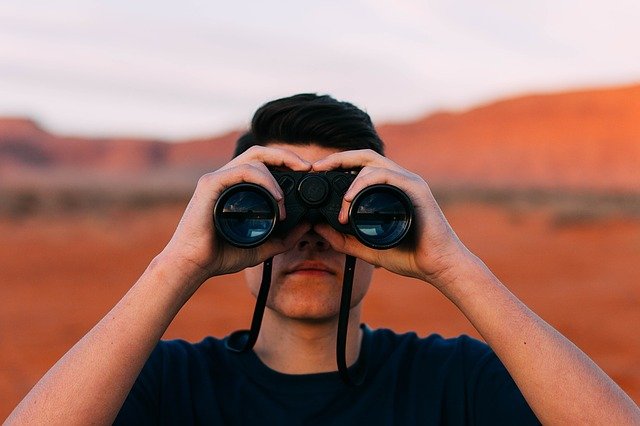 man looking through binoculars focusing forward